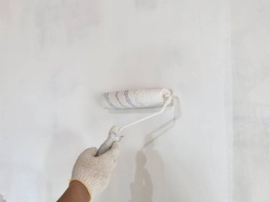 Ressam el ele tutuşup tekerlekli fırça boyayarak yeni bir beyaz duvar boyayarak, iç döşeme yenileme konsepti oluşturdu.