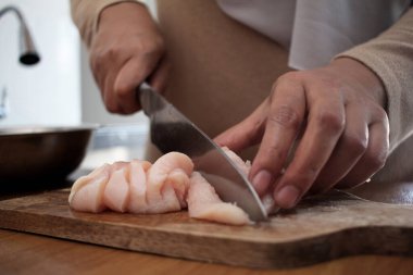 Mutfakta yemek pişirmek. Asyalı Müslüman kadın tavuk göğsü eti kesiyor. Yemek hazırlığı