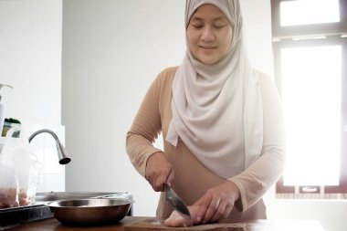 Mutfakta yemek pişirmek. Asyalı Müslüman kadın tavuk göğsü eti kesiyor. Yemek hazırlığı