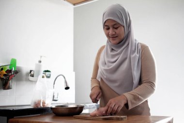 Mutfakta yemek pişirmek. Asyalı Müslüman kadın tavuk göğsü eti kesiyor. Yemek hazırlığı