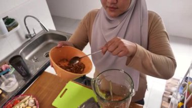 Mutfakta yemek pişirmek. Asyalı Müslüman kadın otlarla baharatları karıştırıyor.