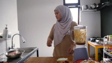 Mutfakta yemek pişirmek. Asyalı Müslüman kadın blenderdan baharat ve otları kasedeki tavuk etinin üzerine döküyor, terbiye süreci