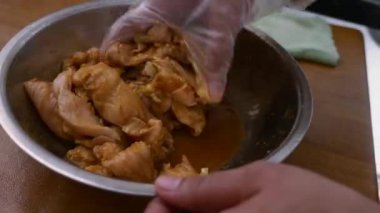 Mutfakta yemek pişirmek. Metal kasede tavuk etini terbiye eden birinin elini kapat.