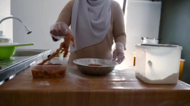 Mutfakta yemek pişirmek. Asyalı Müslüman kadın tavuk pişiriyor. Kızartmadan önce eti unla kaplıyor.