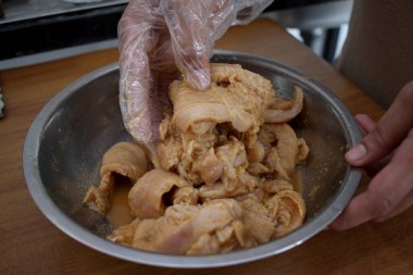 Mutfakta yemek pişirmek. Metal kasede tavuk etini terbiye eden birinin elini kapat.