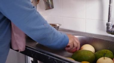 Asyalı Müslüman kadın mutfak lavabosunda meyve yıkıyor, yemek hazırlıyor.