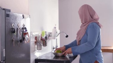 Asyalı Müslüman kadın mutfak lavabosunda meyve yıkıyor, yemek hazırlıyor.
