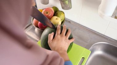 Asyalı Müslüman kadın mutfakta karpuz dilimliyor, yemek hazırlıyor.