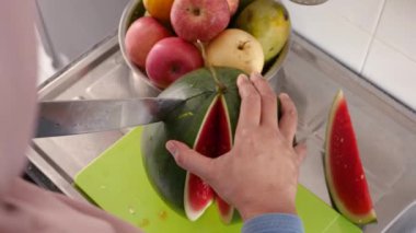 Asyalı Müslüman kadın mutfakta karpuz dilimliyor, yemek hazırlıyor.