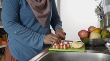Asyalı Müslüman kadın mutfakta elma ve armut dilimliyor, yemek hazırlıyor.