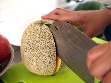 Asyalı Müslüman kadın mutfakta karpuz dilimliyor, yemek hazırlıyor.