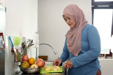 Asyalı Müslüman kadın mutfakta elma ve armut dilimliyor, yemek hazırlıyor.