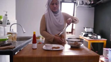 Asyalı Müslüman kadın beyaz tabakta kızarmış tavuk ve ketçap ya da acı sos servis ediyor.