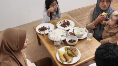 Asyalı Müslüman bir aile yemek yerken sohbet ediyor, yemek masasında oturuyor, mutlu bir aile.