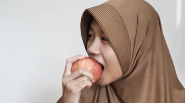 Dişleri diş teli olan, elma yiyen Asyalı Müslüman kadının yakın plan fotoğrafı. Lezzetli taze meyve, yüz ifadesi.