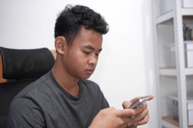 İşitme cihazı olan genç Asyalı çocuk telefon kullanıyor.