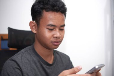 İşitme cihazı olan genç Asyalı çocuk telefon kullanıyor.