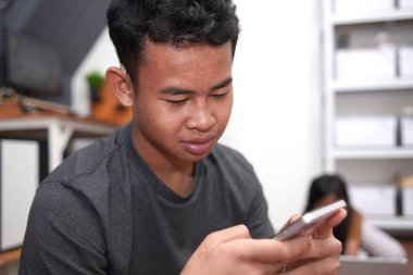 İşitme cihazı olan genç Asyalı çocuk telefon kullanıyor.