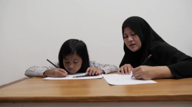 Asyalı Müslüman anne kızıyla oynayıp resim yapmayı öğreniyor, evde ebeveyn eğitimi dersi veriyor.
