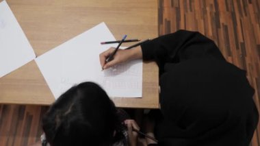 Asyalı Müslüman anne kızıyla oynayıp resim yapmayı öğreniyor, evde ebeveyn eğitimi dersi veriyor.