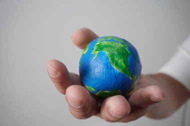 Gri arkaplan üzerinde, boyalı toptan yapılmış yeşil mavi dünya küresi tutuyordu.