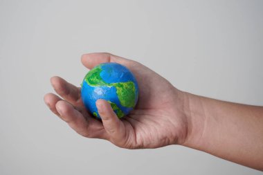 Gri arkaplan üzerinde, boyalı toptan yapılmış yeşil mavi dünya küresi tutuyordu.