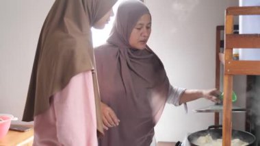 Endonezyalı Müslüman kadın kızıyla mutfakta yemek hazırlıyor, geleneksel otantik Asya yemekleri pişiriyor, doğal ışık.