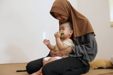 Asyalı Müslüman ablası bebeğine bakıyor, onu rahatlatıyor ve besliyor, bebek bakıcılığı yapıyor.