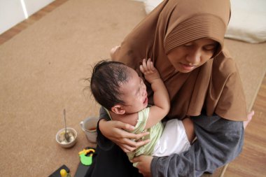 Asyalı Müslüman ablası bebeğine bakıyor, onu rahatlatıyor ve besliyor, bebek bakıcılığı yapıyor.