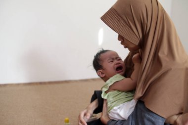 Asyalı Müslüman ablası bebeğine bakıyor, onu rahatlatıyor ve besliyor, bebek bakıcılığı yapıyor.