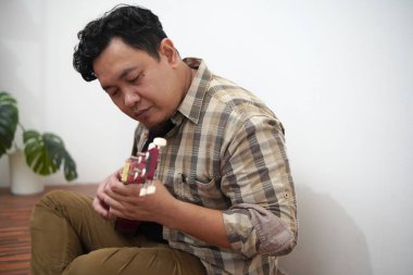 Asian man playing ukulele at home, sit on floor clipart