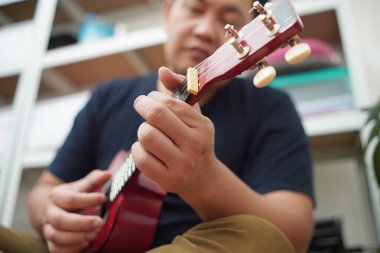 Asian man playing ukulele at home, sit on floor clipart