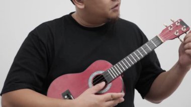 Ukulele tellerini ayarlayan Asyalı adam