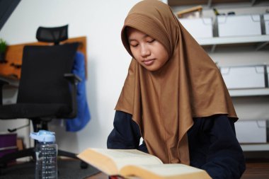 Genç Asyalı Müslüman kadın evde kitap okuyor, mutlu gülümseyen akıllı kişi. Eğitici kavram