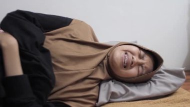 Genç Asyalı Müslüman kadın yüzünü buruştururken ve sıkarken acı içinde yatıyor, mide ağrısı konsepti.