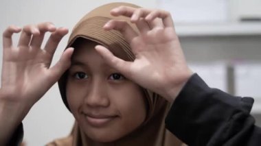 Genç Asyalı Müslüman kadın aynanın önünde duruyor, başörtüsünü ya da başörtüsünü takıyor