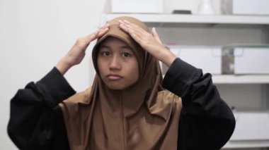 Genç Asyalı Müslüman kadın aynanın önünde duruyor, başörtüsünü ya da başörtüsünü takıyor