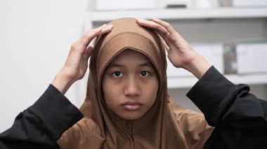 Genç Asyalı Müslüman kadın aynanın önünde duruyor, başörtüsünü ya da başörtüsünü takıyor