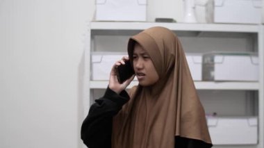 Genç Asyalı Müslüman kadın telefonda konuşurken kafası karışık ve üzgün görünüyor. Kötü haber kavramı alıyor.