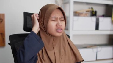 Genç Asyalı Müslüman kadın bilgisayarın önünde otururken şaşkın görünüyor.