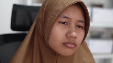 Genç Asyalı Müslüman kadın tesettürlü bilgisayar monitörüne ciddi ciddi bakıyor, bilgisayar üzerinde çalışan kişi