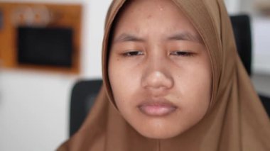 Genç Asyalı Müslüman kadın tesettürlü bilgisayar monitörüne ciddi ciddi bakıyor, bilgisayar üzerinde çalışan kişi