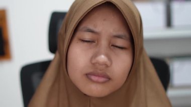 Genç Asyalı Müslüman kadın kameraya bakıyor, ciddi bir ifade.