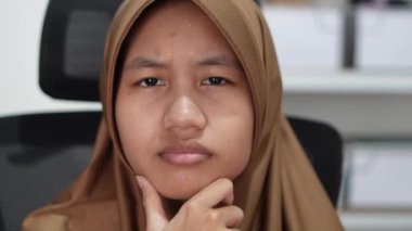 Genç Asyalı Müslüman kadın kameraya bakıyor, ciddi bir ifade.