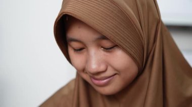 Genç Asyalı Müslüman kadın tesettüre girmiş, diş teli takmış kameraya bakıyor ve gülümsüyor. Mutlu ifade