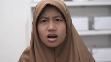 Genç Asyalı Müslüman kadın şok olmuş bir ifadeyle kameraya bakıyor, ağzı açık.