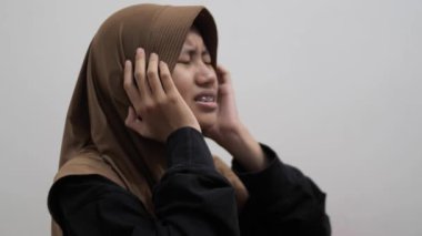 Genç Asyalı Müslüman kadın kafasına dokunuyor, keder ifadesi, baş ağrısı jesti.