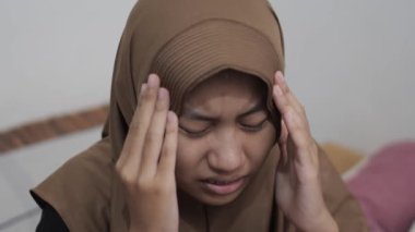 Genç Asyalı Müslüman kadın kafasına dokunuyor, keder ifadesi, baş ağrısı jesti.