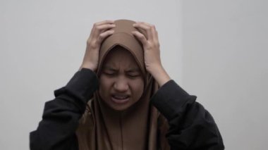 Genç Asyalı Müslüman kadın kafasına dokunuyor, keder ifadesi, baş ağrısı jesti.