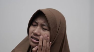 Genç Asyalı Müslüman kadın, diş ağrısından dolayı yanağını tutuyor. Diş sağlığı konsepti